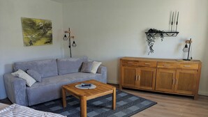 A living room with a sofa, a coffee table, a cabinet, and a painting on the wall. - Holiday apartment Collis in our guesthouse in the old town of Zell (Moselle) (Zell (Mosel))