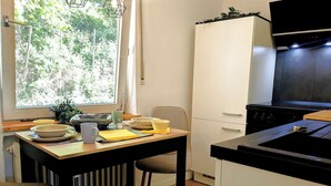 A kitchen with a dining table, chairs, a stove, and a window with a view of trees. - Holiday apartment Collis in our guesthouse in the old town of Zell (Moselle) (Zell (Mosel))