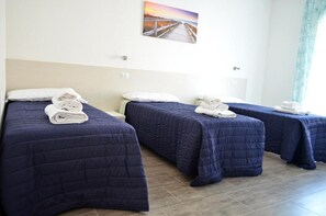 A hotel room with three beds, each with a blue quilt and white towels. There is a painting of a sunset on the wall. - B&b Eden Ogliastra  (Tortolì)