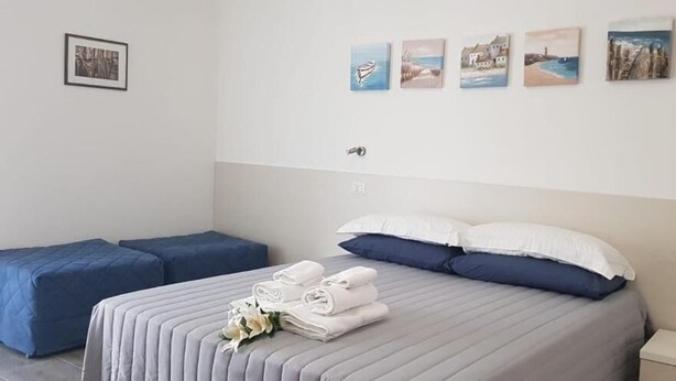 A hotel room with a bed, two blue sofas, a bedside table, and a wall with four framed pictures. - B&b Eden Ogliastra  (Tortolì)