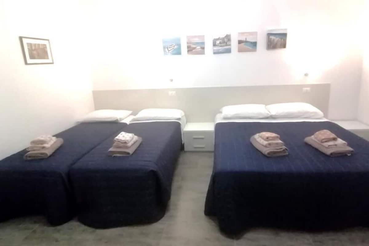 Une chambre avec deux lits, chacun étant équipé d’un oreiller et d’une serviette pliée. Des tableaux sont accrochés au mur au-dessus des lits.