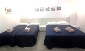 A room with two beds, each with a pillow and a folded towel. There are wall-mounted pictures above the beds. - B&b Eden Ogliastra  (Tortolì)