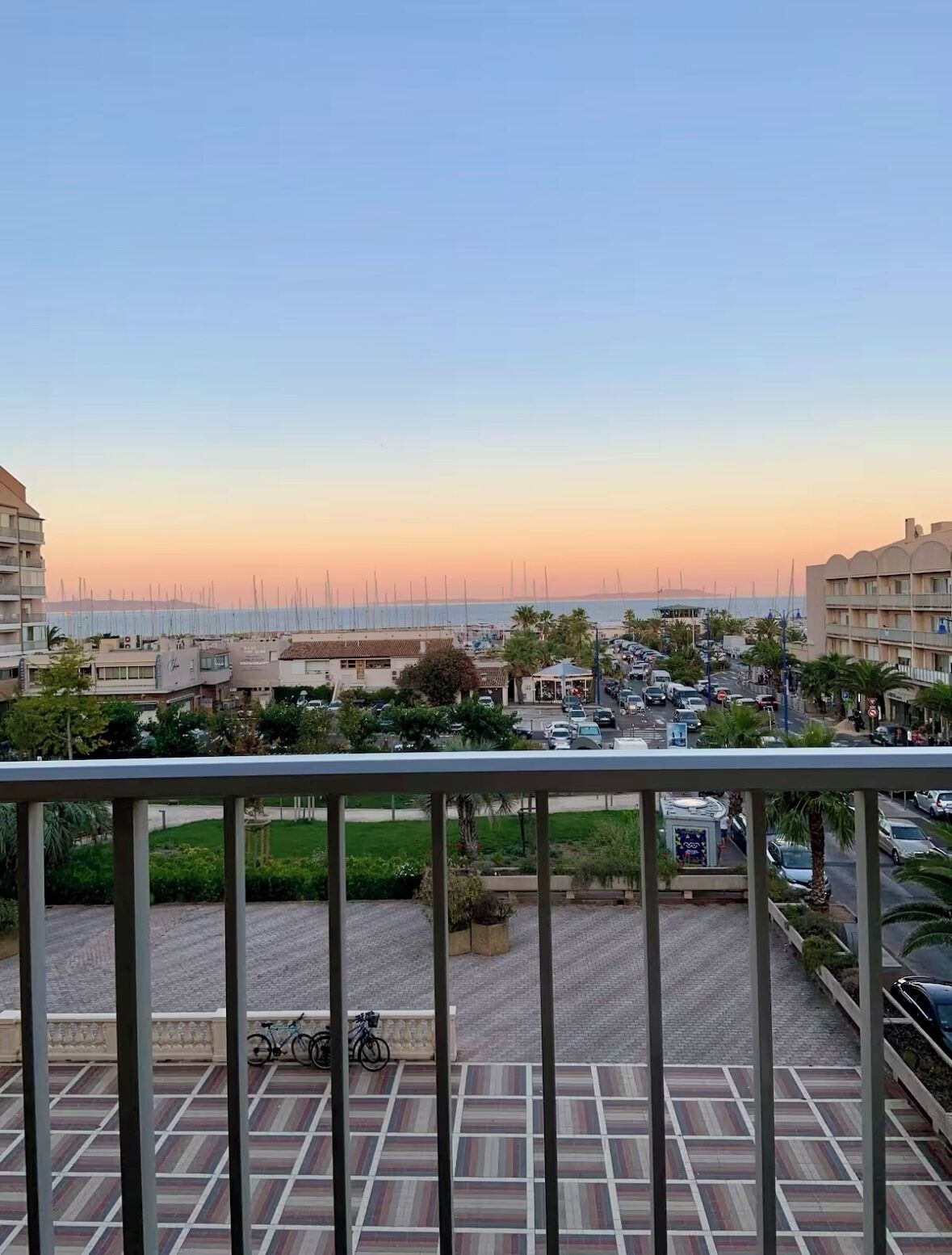 Un balcon avec vue sur un port de plaisance, des immeubles et un parking.