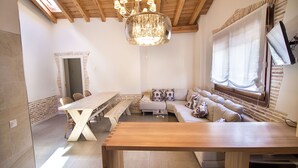 Un intérieur moderne avec un plafond en bois, un lustre, un ensemble de canapés, une table à manger et un téléviseur.