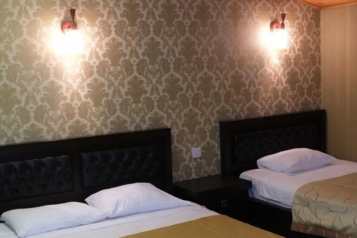 A room with two beds, wooden ceiling, patterned wallpaper, and wall-mounted lights.