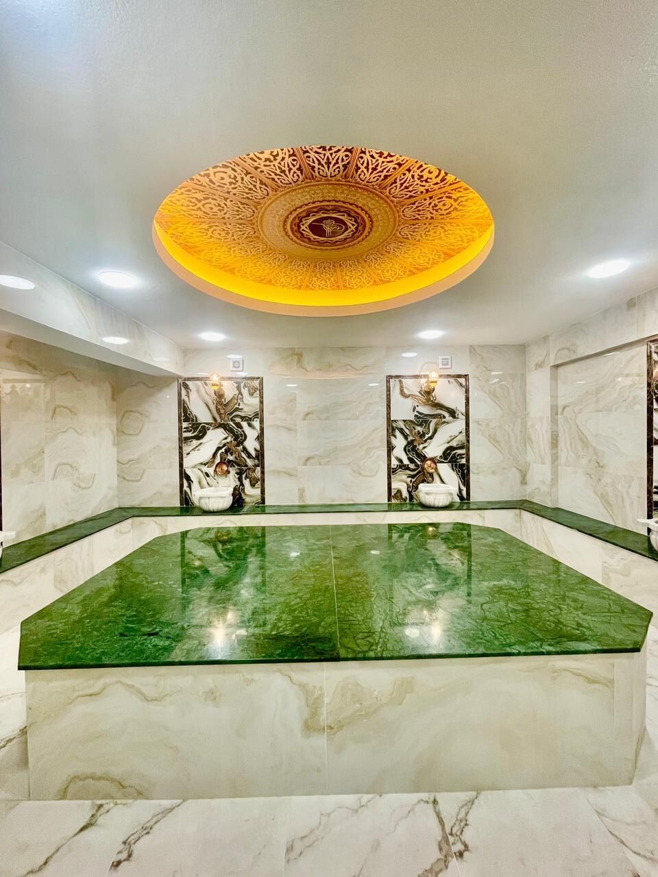 A hotel lobby with a green marble reception desk, marble walls with intricate patterns, and a decorative ceiling.
