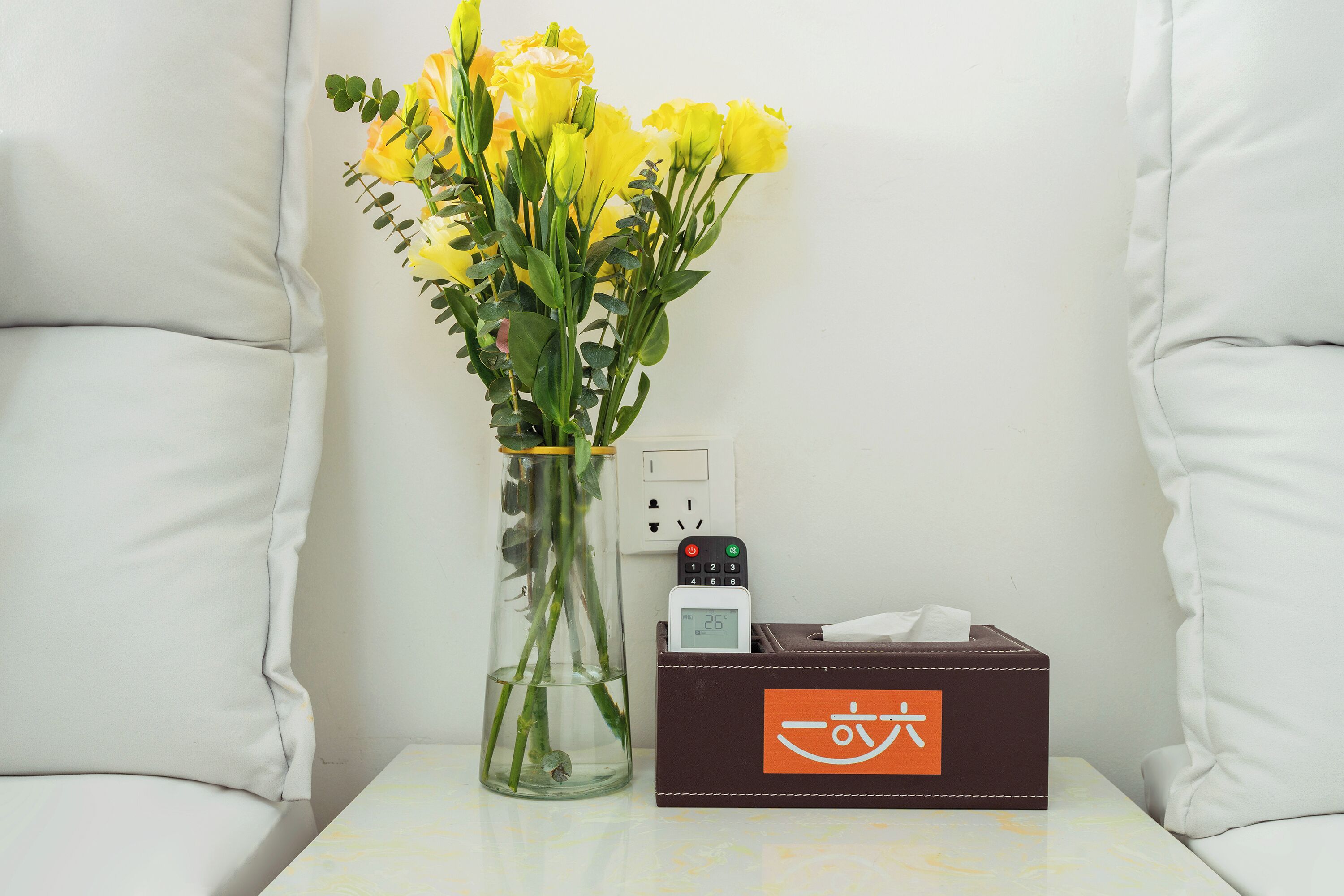 Un jarrón con flores amarillas sobre una mesa junto a una caja con un logotipo.