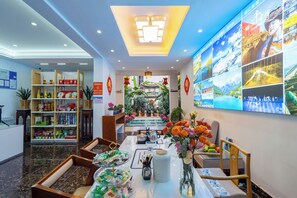 A hotel lobby with a reception desk, a dining area with a table set for two, and a view of a garden through the glass wall. - 166 Hotel-Ancient City Mufu Branch (Lijiang)