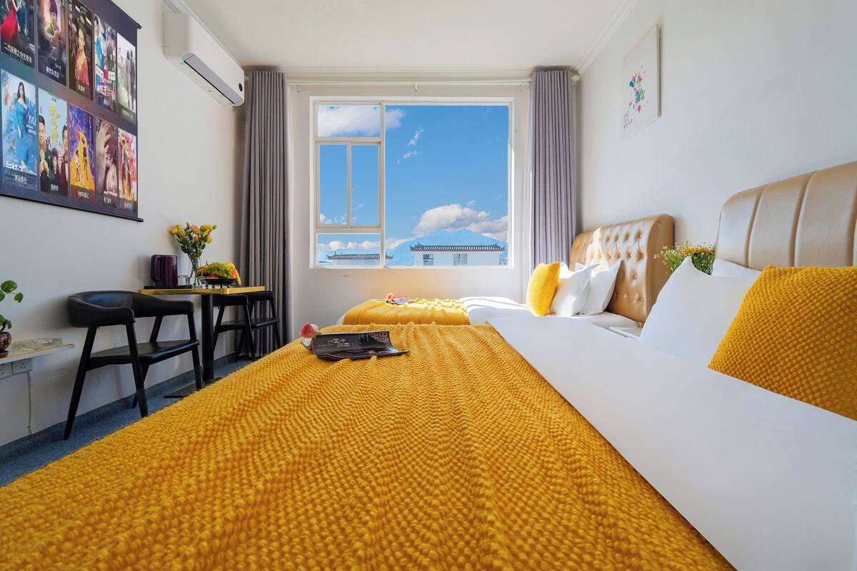 Ein Hotelzimmer mit einem großen Bett, einem Schreibtisch mit Stühlen, einem Fenster mit Blick auf ein traditionelles Gebäude und einem Poster an der Wand.