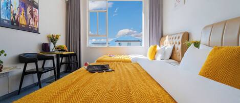 A hotel room with a large bed, a desk with chairs, a window with a view of a traditional building, and a poster on the wall.