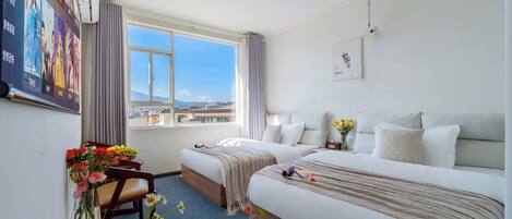 A hotel room with two beds, a desk with a chair, a large window, and a view of the city.