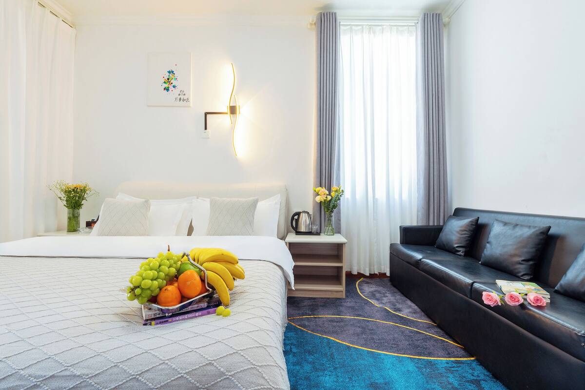 Ein Hotelzimmer mit einem Bett, einem schwarzen Ledersofa, einem Nachttisch mit Blumenvase und einer wandmontierten Lampe.