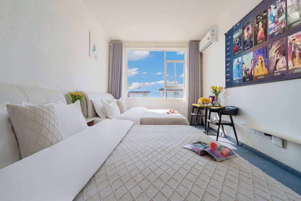 Ein Hotelzimmer mit zwei Betten, einem Schreibtisch, einem Sessel, einem Fenster mit Blick und einer Wand voller Filmplakate.