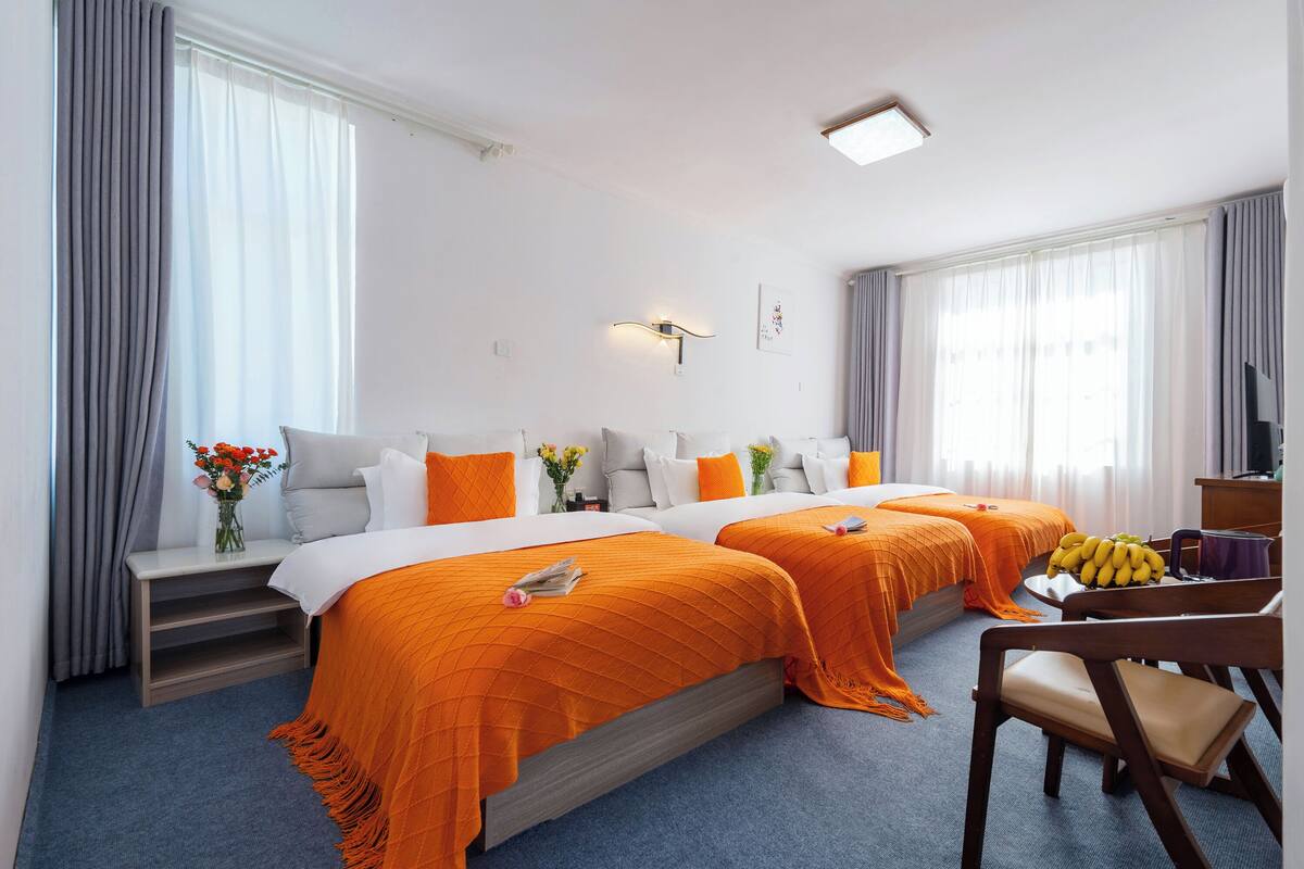 Ein Hotelzimmer mit zwei Betten, einem Schreibtisch, einem Stuhl, einem Fernseher und einem Fenster mit Vorhängen.