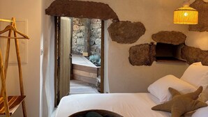 Quarto com cama, luminária pendente, cabide de madeira e parede de pedra.