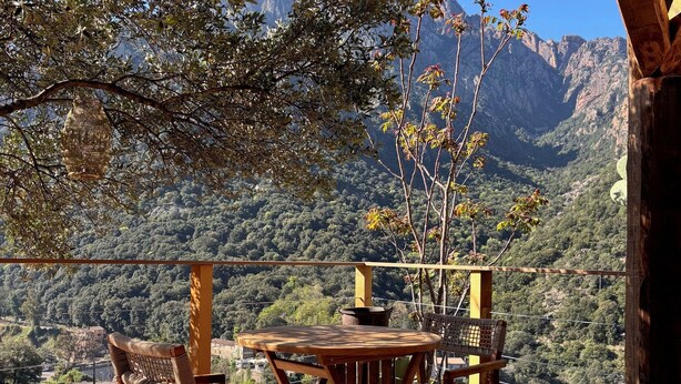 Um deck de madeira com mesa e cadeiras, com vista para uma paisagem montanhosa.