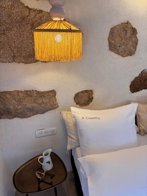 A bedroom with a bed, a bedside table with a mug, a wall-mounted lamp, and a power outlet. - At Casetta, a suspended moment in a green setting (Ota)