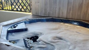 Un bain à remous avec une terrasse en bois et une clôture métallique en arrière-plan.