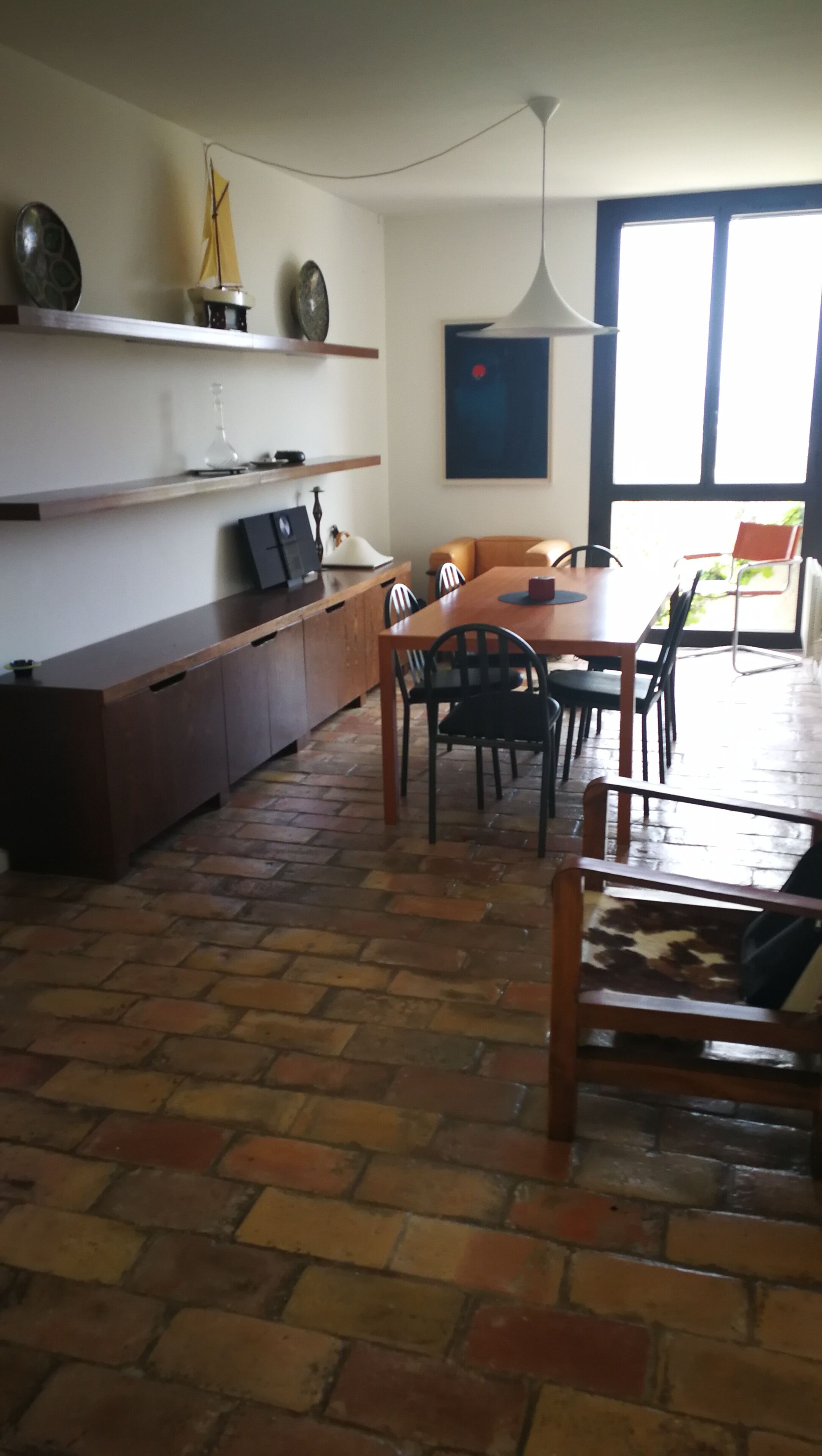 A dining area with a brick floor, wooden furniture, and a modern pendant light.