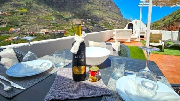 A table set for dining with a bottle of wine, glasses, and plates, overlooking a mountainous landscape. - Casa Lara Hermigua - Superior Apartment with a large terrace (Hermigua)