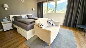 A bedroom with a bed, a sofa, a nightstand, a lamp, a window with curtains, and a view of mountains. - Casa Lara Hermigua - Superior Apartment with a large terrace (Hermigua)