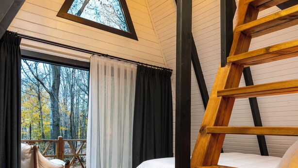 A loft bedroom with a wooden ladder, a large window, and a view of trees. - Suma Disanje Boutique Hotel (Sile)