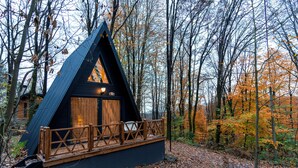 A cabin with a wooden deck and a triangular roof, surrounded by trees. - Suma Disanje Boutique Hotel (Sile)