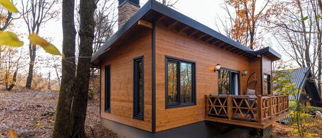 A wooden cabin with a deck, large windows, and a chimney.