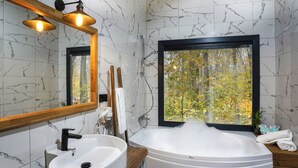 A modern bathroom with a marble wall, a bathtub with bubbles, a wooden vanity, a large mirror, and a window with a view of trees. - Suma Disanje Boutique Hotel (Sile)