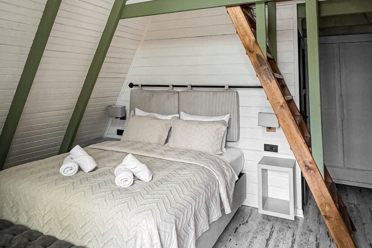 Une chambre à coucher aménagée dans un espace en hauteur, comprenant un lit, des tables de chevet, un banc et un luminaire suspendu.