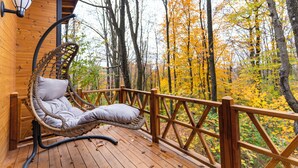A wooden deck with a wicker swing chair and a view of autumn trees. - Suma Disanje Boutique Hotel (Sile)
