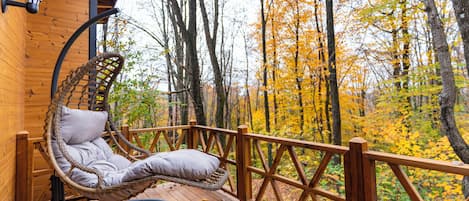 A wooden deck with a wicker swing chair and a view of autumn trees.