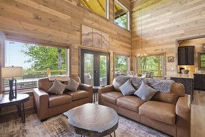 Ein gemütliches Blockhauss-Interieur mit Holzbalkendecke, einer Sofagarnitur, einem Esstisch und einer Küchenzeile.