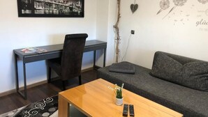Una habitación con un escritorio, un sofá, una mesa de centro, un cuadro en la pared, una rama decorativa y una obra de arte mural.