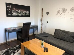 A room with a desk, a sofa, a coffee table, a wall-mounted picture, a decorative branch, and a wall art piece. - Fine vacation apartment Bayreuth (Bayreuth)