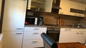 Una cocina moderna con armarios blancos, horno empotrado, cafetera y tabla de cortar de madera.
