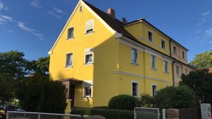 Un edificio amarillo de dos pisos con varias ventanas, una puerta visible y una antena parabólica pequeña en el techo.
