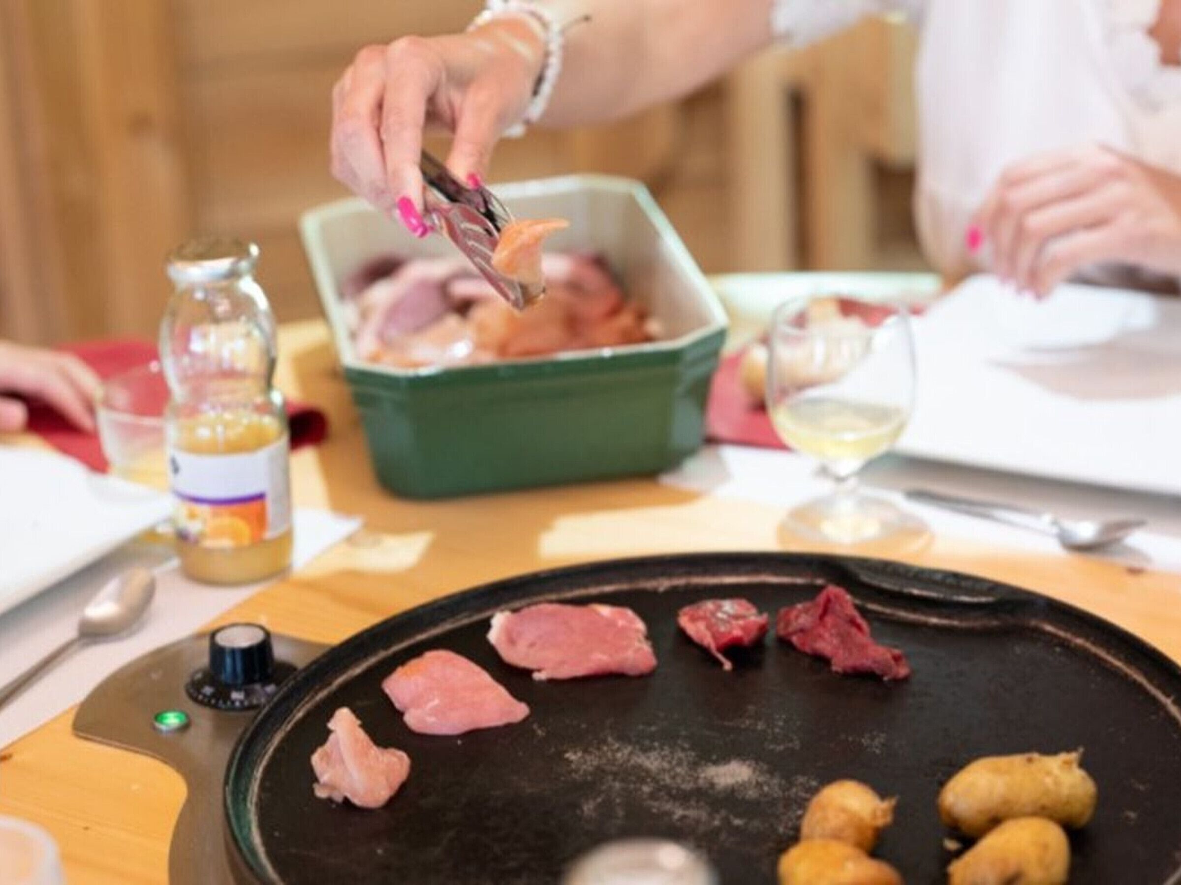 En person som tillagar mat på en grill, med rått kött och grönsaker.