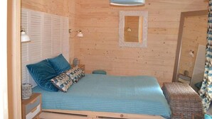 A wooden room with a bed, a small table, a hanging light fixture, and a window with shutters. - Cozy chalet - 6 guests (Magné)