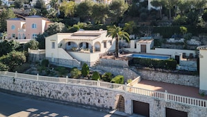 Una villa de estilo mediterráneo con piscina, muros de piedra y vistas del barrio circundante.
