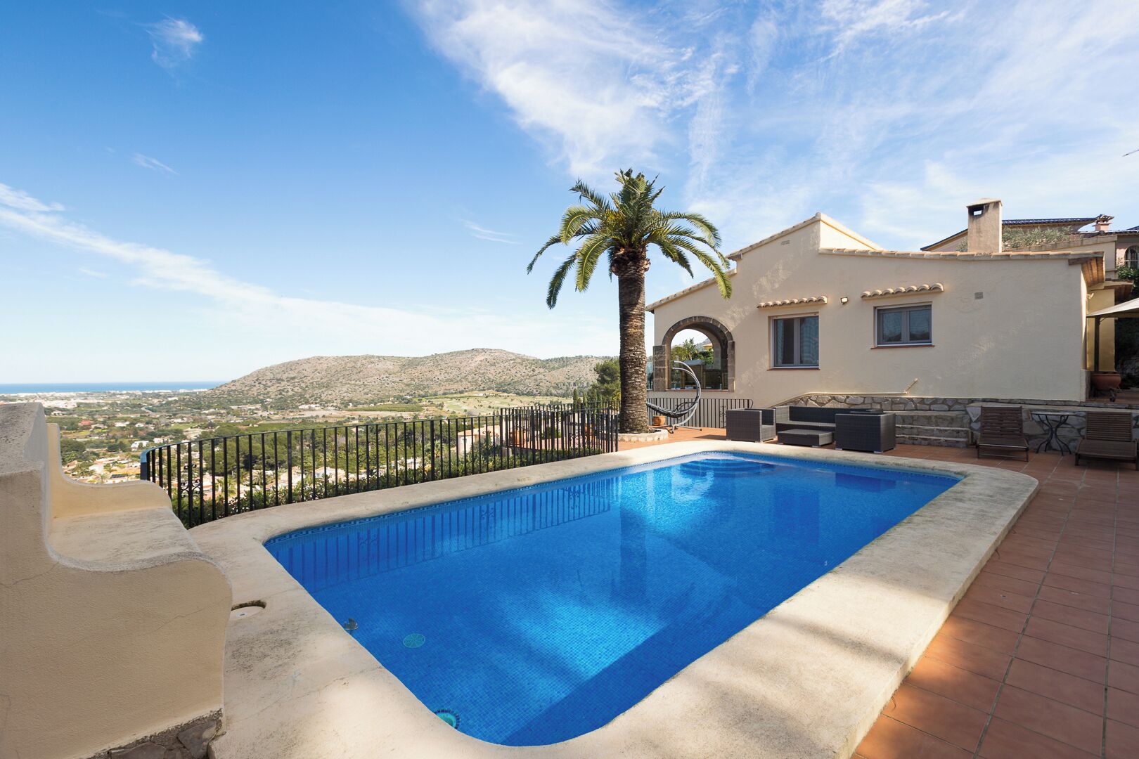 Une piscine avec vue sur un paysage montagneux, un palmier et un bâtiment doté d’un balcon.