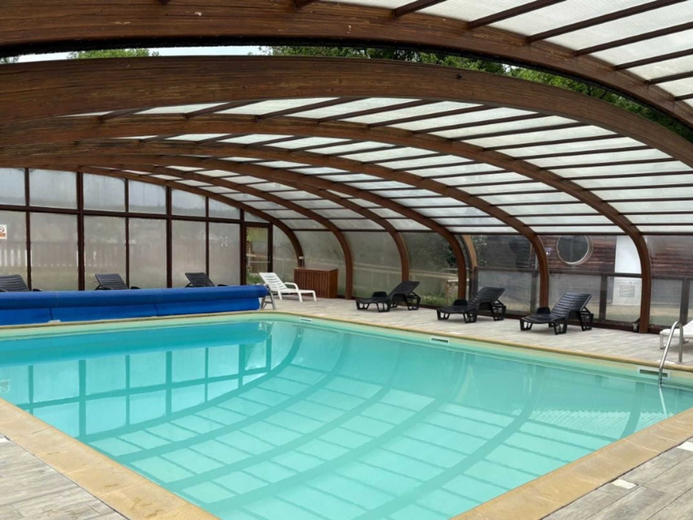 Ein überdachter Pool mit Liegestühlen und einer blauen Sitzbank.