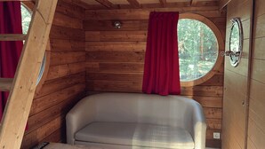 Ein Holzinnenraum einer Hütte mit einem runden Fenster, einem roten Vorhang und einer weißen Badewanne.