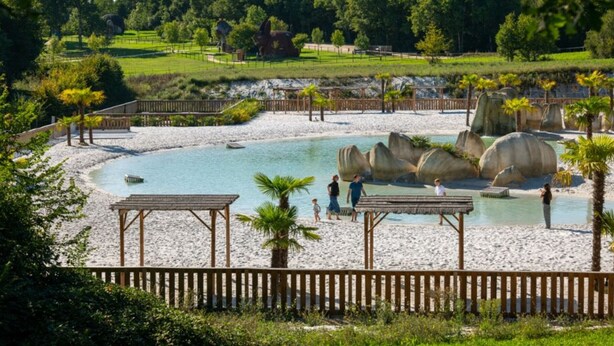 Ein Strandbereich mit Pool, Palmen und einem Holzzaun.