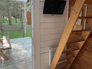 Interior de madera con un televisor montado en la pared, una escalera y vistas al exterior.
