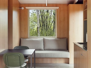 Ein Zimmer mit einer Holzwand, einem Fenster mit Blick auf Bäume, einem Sofa, einem Tisch und einem Stuhl.