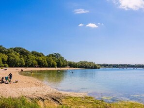 A beach with people, a boat, and a forested area in the background. - Mobile home with AC - 2 guests (Arrigny)