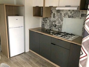 Una cocina compacta con refrigerador, estufa a gas, gabinetes oscuros y salpicadero con diseño.