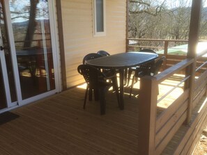 A covered patio with a wooden deck, a round table, and four chairs. - Cozy chalet - 5 guests (Vogüé)