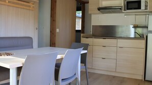 A compact kitchen with a microwave, stove, and cabinets. There is a dining table with chairs and a bench.